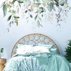 a bed with green comforters and pillows in front of a wall painted with watercolor leaves