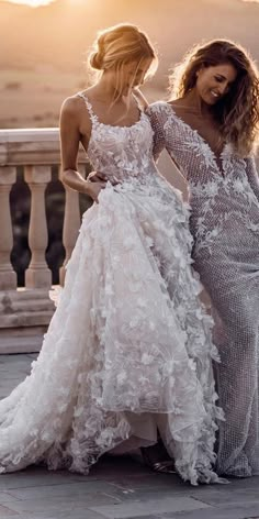 two beautiful women standing next to each other on a balcony with the sun setting in the background