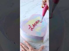 someone is decorating a heart shaped cake with the word love spelled in pink icing