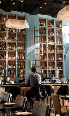 a man sitting at a bar with lots of bottles on the shelves in front of him