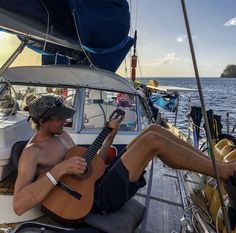 a man sitting on top of a boat while playing a guitar