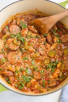 a pot filled with meat and vegetables next to a wooden spoon on top of a table