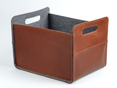 a brown leather storage bin with handles on the side and grey felt lining around it