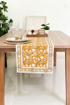 a dining table with an orange and white table runner on top of it, next to a potted plant