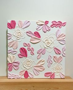 a white and pink flowered card on a wooden shelf next to a vase with flowers in it