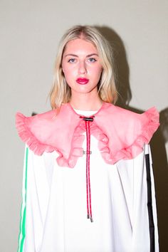 a woman with blonde hair wearing a white shirt and pink ruffle collared top