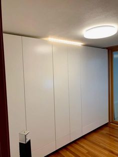 an empty room with white cupboards and wood flooring in front of a window