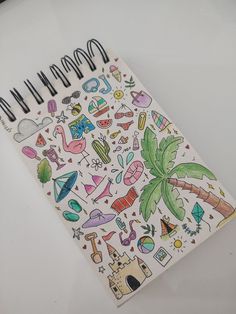 an open notebook with drawings on the pages and palm trees, buildings, and other items