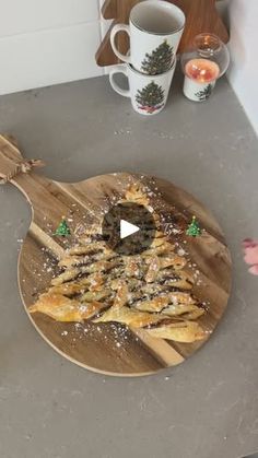 a wooden cutting board topped with pizza on top of a counter next to cups and saucers