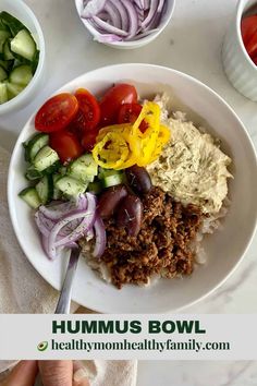 a bowl filled with meat, vegetables and hummus on top of a white table