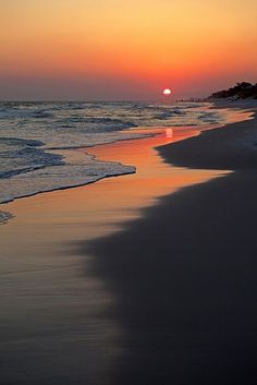 the sun is setting over the water at the beach with waves coming in to shore