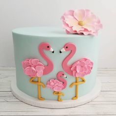 a blue cake with pink flowers and two flamingos on the top is sitting on a white table