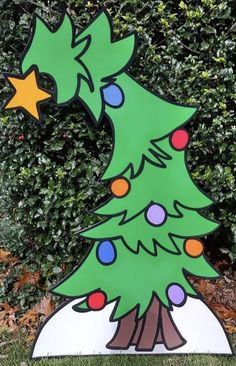 a wooden christmas tree with lights on it in front of some bushes and shrubbery