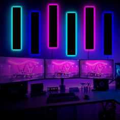 three computer monitors sitting on top of a desk in front of neon colored wallpaper