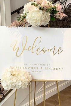 a welcome sign sitting on top of a metal stand with flowers in front of it