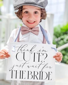 a little boy in a hat and bow tie holding a sign that says here comes the bride