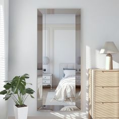 a white bedroom with a large mirror in the corner and a plant on the floor