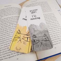 two bookmarks with cats on them sitting next to an open book