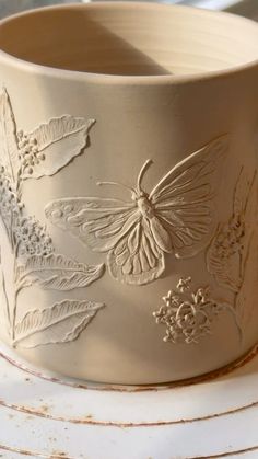 a close up of a bowl on a table with flowers and butterflies painted on it