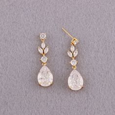 two pairs of diamond earrings on a gray surface, one is gold and the other is white