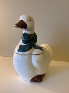 a ceramic duck with a blue bow on its neck sitting on a table next to a white wall