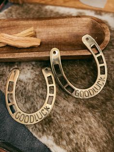 a pair of gold horseshoe shaped earrings sitting on top of a cowhide rug next to a wooden tray