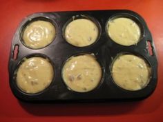 a muffin tin filled with yellow batter on top of a red table next to a cupcake pan