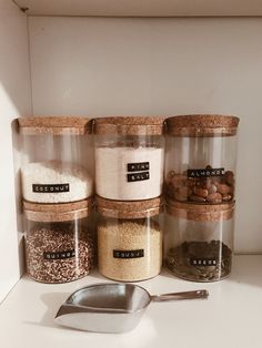 four jars with different types of food in them on a counter next to a spoon