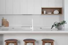 three stools in front of a counter top with white cupboards and shelves above it