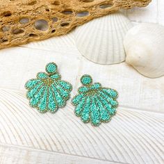 two pairs of green beaded earrings sitting on top of a white table next to shells