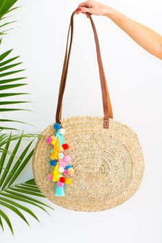 a straw bag with colorful tassels hanging from it's side and a palm tree in the background