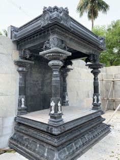 an old stone structure with statues on the sides and pillars around it, in front of a concrete wall