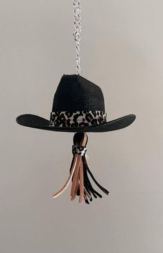 a black hat hanging from a chain with tassels on the ends and an animal print band around the brim