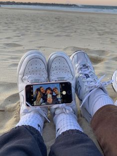 someone taking a selfie with their cell phone on the beach while wearing tennis shoes