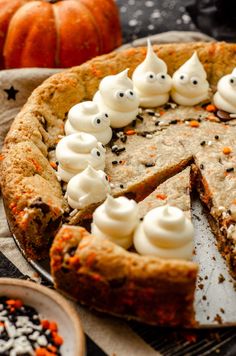 a pumpkin pie with white frosting and sprinkles on it, sitting on a table