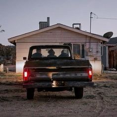 two people are sitting in the back of a pick - up truck on a dirt road