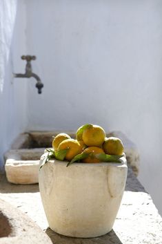 a white bowl filled with oranges sitting on top of a counter next to a faucet