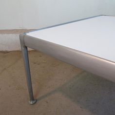 a white table sitting on top of a cement floor next to a metal frame wall