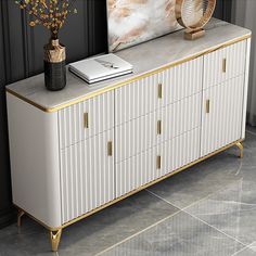 a white and gold sideboard with two vases on it next to a painting