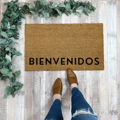 a woman standing in front of a welcome mat with the word welcome on it and greenery around her