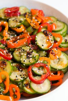 a white bowl filled with sliced up cucumbers and red bell peppers, topped with sesame seeds