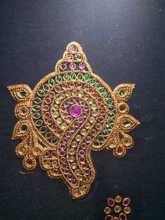 an intricately designed gold brooch with pink and green stones on it's side