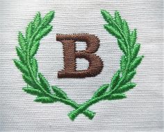 the letter b is embroidered on top of a white cloth with green leaves around it