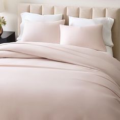 a bed with pink sheets and pillows in a bedroom next to a lamp on a night stand