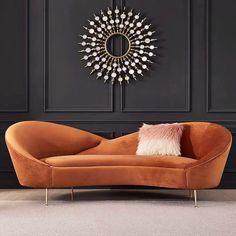 an orange couch sitting in front of a black wall with a gold sunburst mirror on it