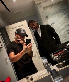 two men standing in front of a mirror looking at their cell phones