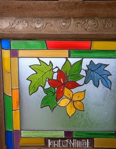 a stained glass window with colorful leaves and words on the bottom panel, in a wood frame