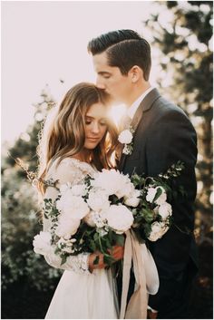 a bride and groom embracing each other in front of some trees with sun shining on them