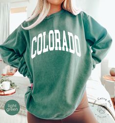 Comfort Colors® Colorado Sweatshirt, Boho, Colorado Crewneck, Colorado Women's Sweatshirt, Colorado Vintage Sweatshirt, Vintage Crewneck Hi, thank you so much for shopping with us! ❤️ ◦ ◦ ◦ ◦ ◦ size and material ◦ ◦ ◦ ◦ ◦ ◦ Comfort Colors® 1566 ◦ Adult Unisex Crewneck Sweatshirt ◦ 80% Ring Spun Cotton / 20% Polyester ◦ 3-end garment-dyed soft ring spun fleece with a 100% cotton face ◦ Comfort Colors garments are pre-shrunk during the garment dye process for almost no shrinkage at home ◦ Twill taped back neck for comfort and durability ◦ Half-moon neck patch on the back ◦ Relaxed fit, side seamed body ◦ The fabric is soft and pleasant to touch, has a subtle luxurious feel ◦ The way that we print our sweatshirts is Direct-to-Garment printing, meaning that the ink is printed INTO the sweatshi Green Crew Neck Tops With Letter Print, Green Sweater With Letter Print In Relaxed Fit, Green Relaxed Fit Sweater With Letter Print, Green Collegiate Long Sleeve Sweatshirt, Green Collegiate Long Sleeve Tops, Collegiate Long Sleeve Green Tops, Collegiate Green Long Sleeve Tops, Green Long Sleeve Collegiate Sweatshirt, Green Long Sleeve Fan Apparel Top