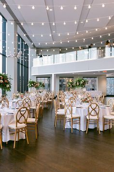 a room filled with tables and chairs covered in white tablecloths next to tall windows